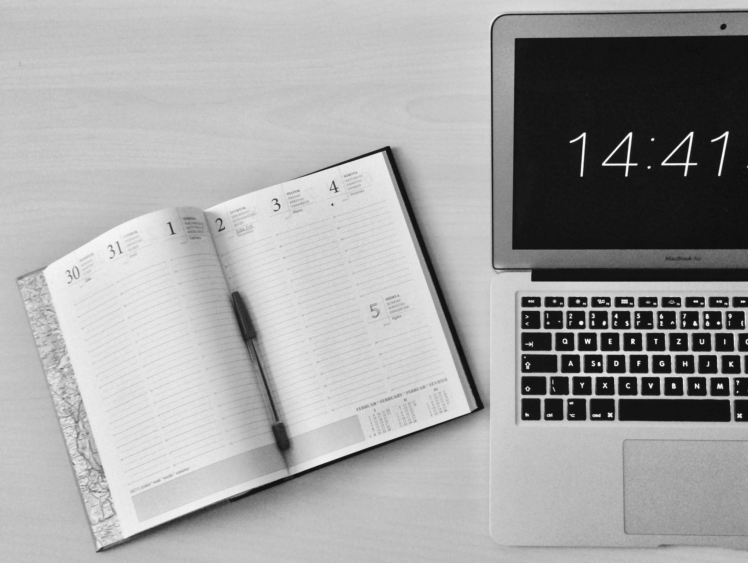 notebook next to laptop with clock on it
