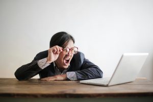 person lifting glasses glaring at laptop