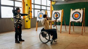 two people practicing shooting a bow and arrow, one in a wheelchair