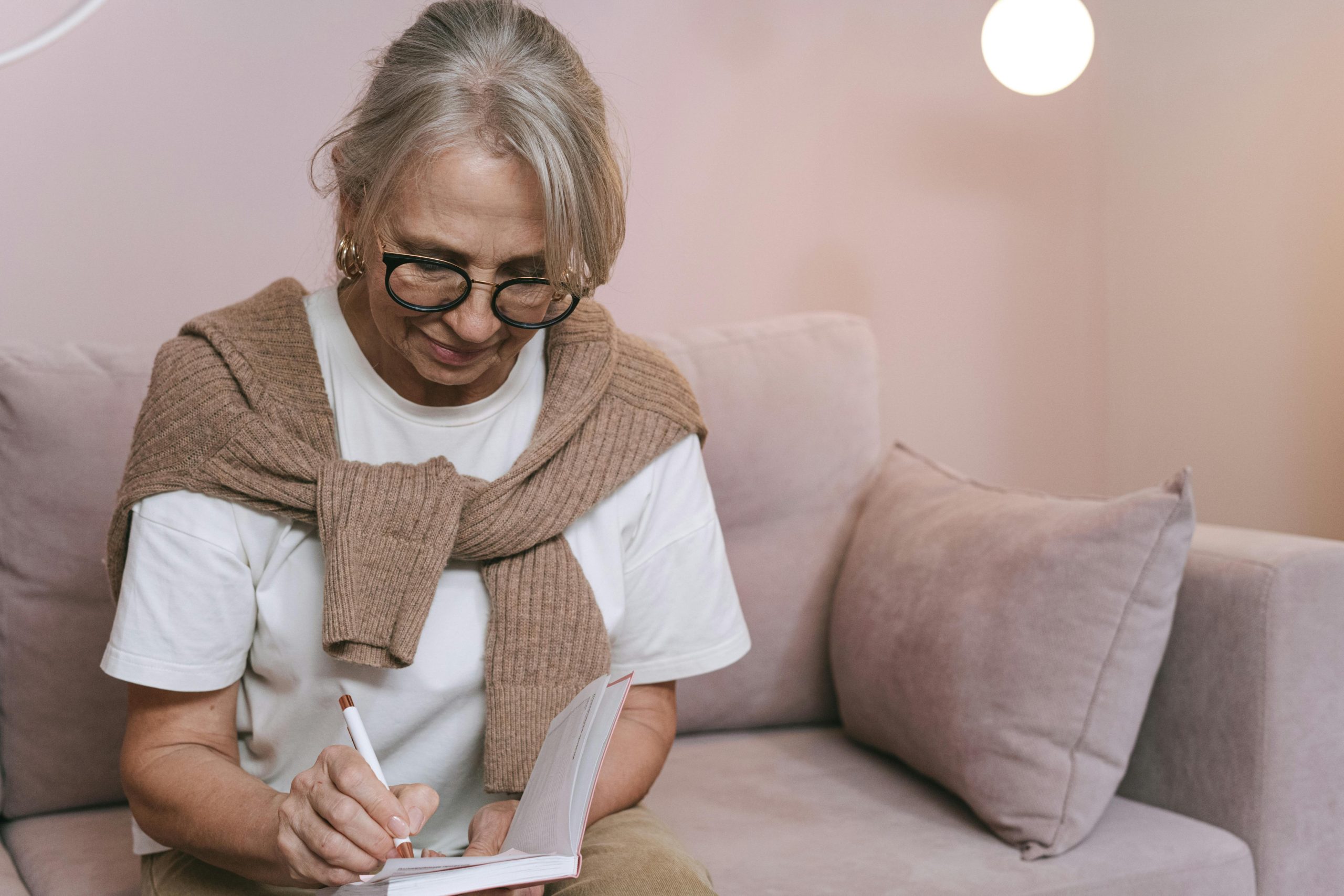 blonde woman writing in journal on couch