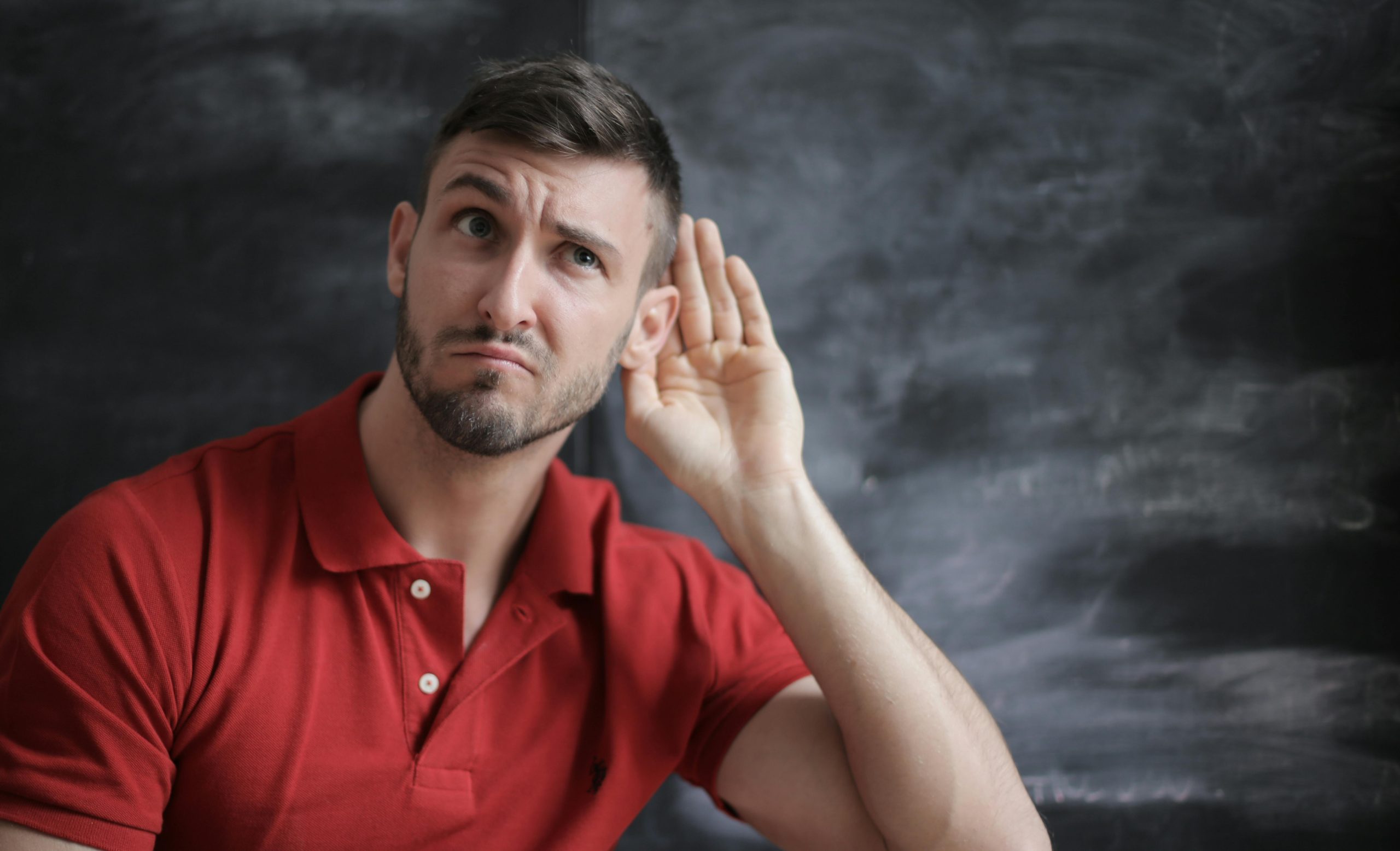 man in red shirt putting his hand to his ear