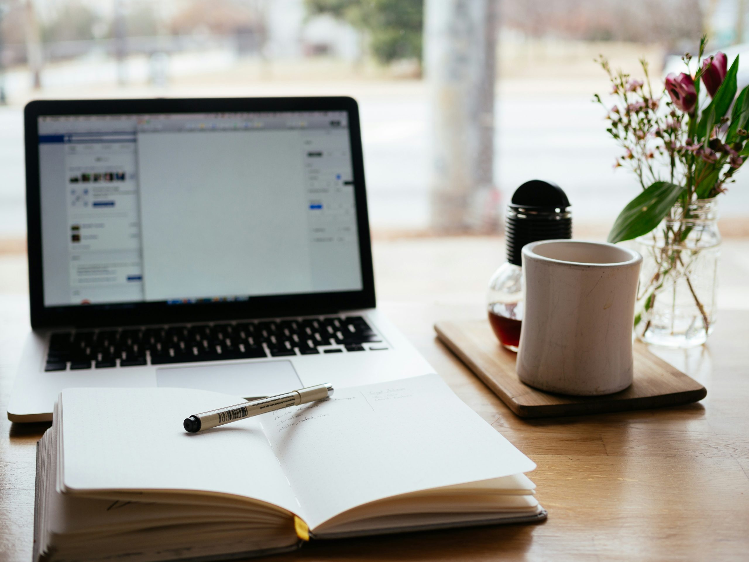 laptop and notebook on desk with coffee and flowers